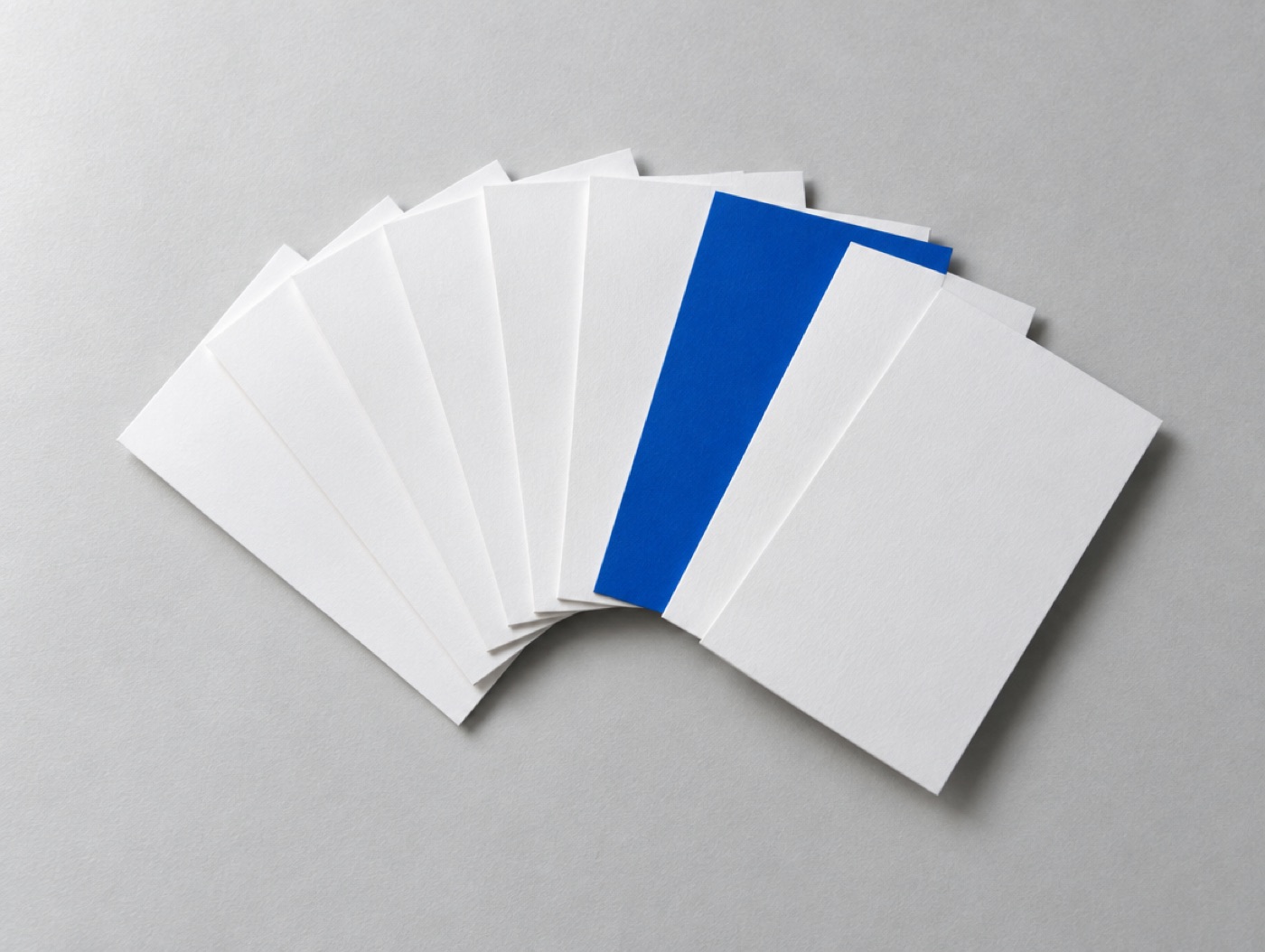 A fan of white cards on a grey surface with one cobalt card among them
