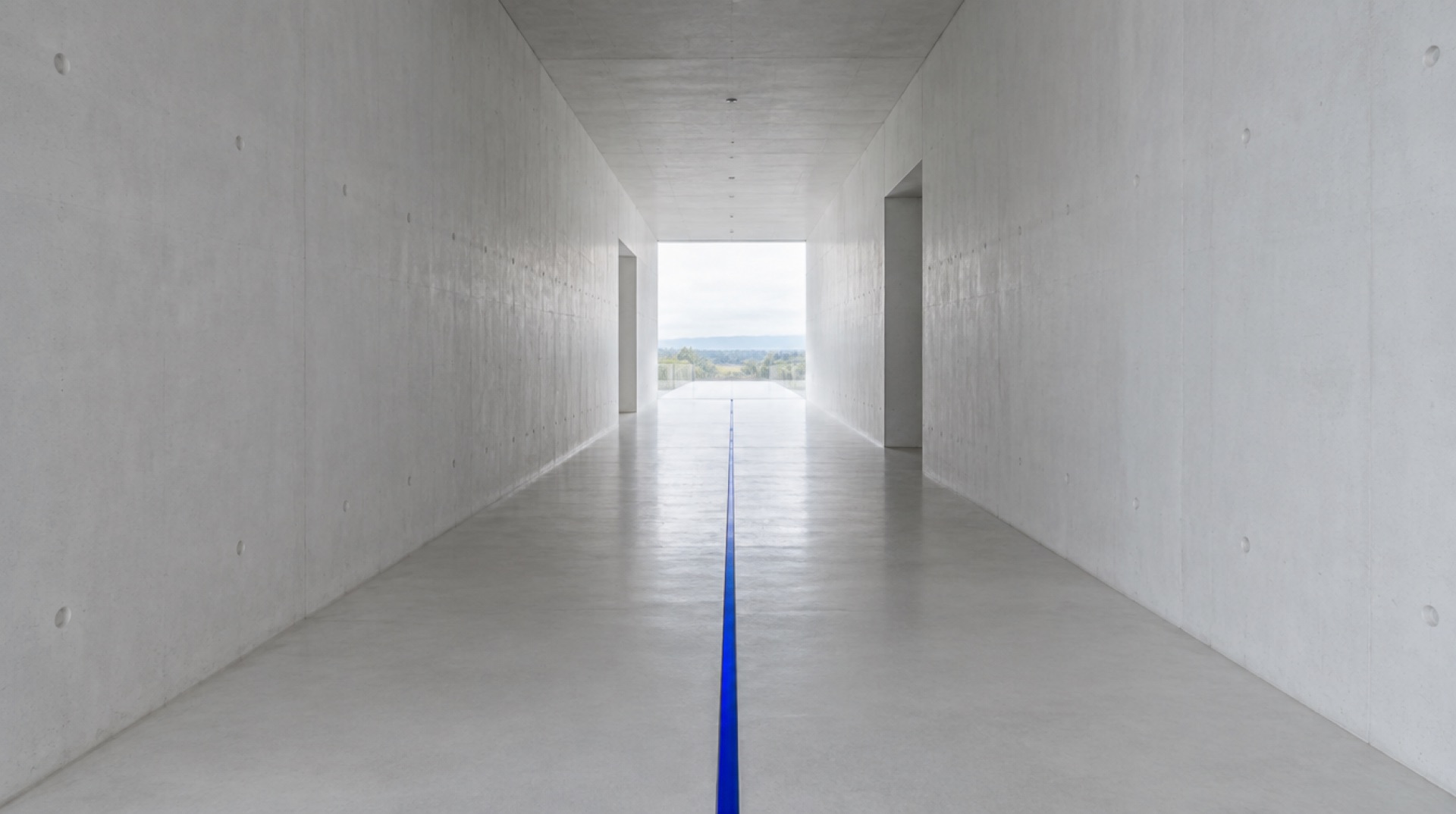A white concrete corridor with a thin line of cobalt light along the floor
